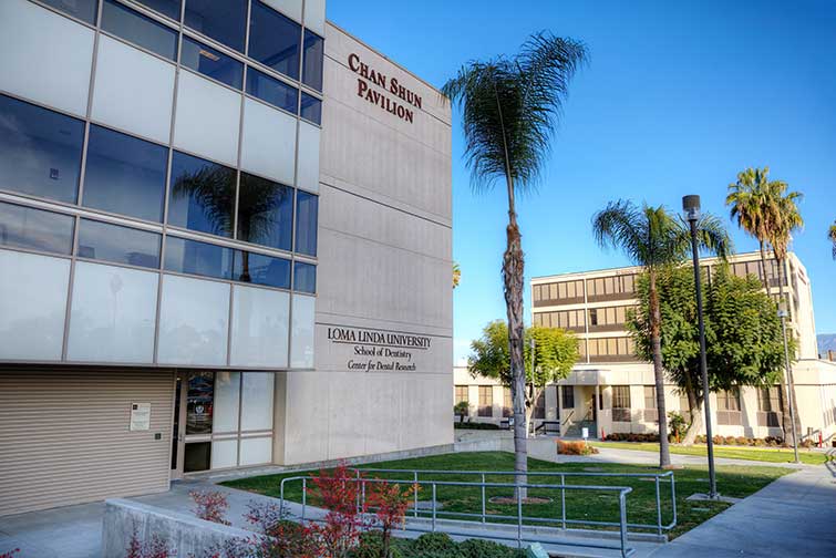 Exterior of the Chan Shun Pavilion at Loma Linda University, a three-story glass and concrete building housing the Center for Dental Research, surrounded by palm trees.