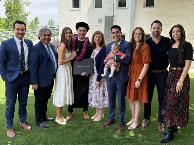 Jason Chan wearing academic regalia holding a diploma folder while standing outdoors with his family
