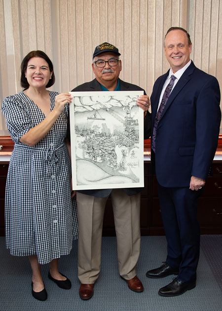 Jen Carson, Mike Gonzalez and Dean Handysides standing indoors holding a unframed lithograph in an office setting