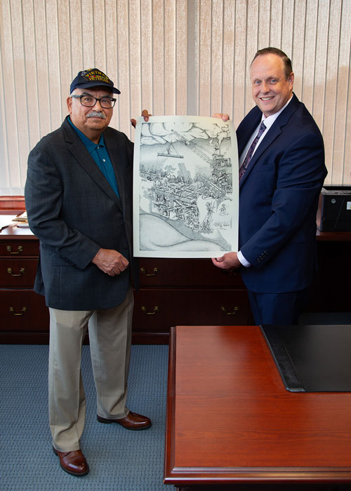 Two people standing indoors holding a unframed lithograph in an office setting