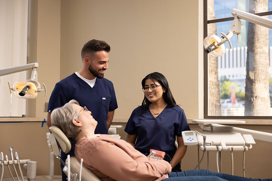 Dental care professionals speaking with a patient seated in a dental chair inside a treatment room.