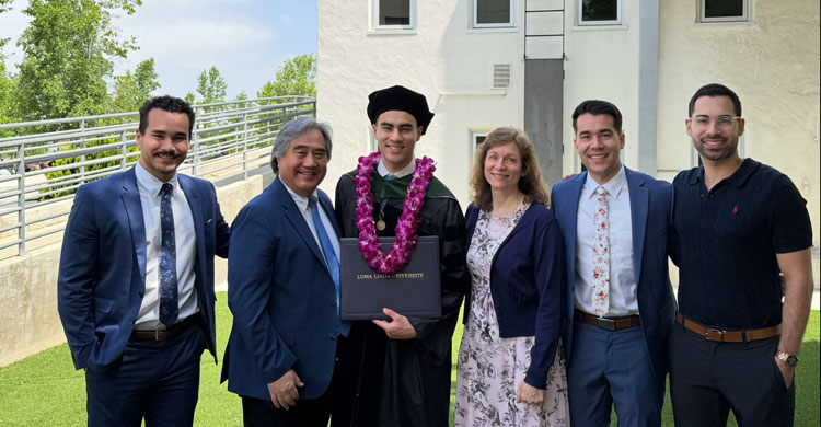 Jason Chan wearing academic regalia holding a diploma folder while standing outdoors with a his family