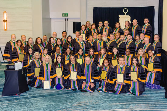 Large group of people wearing ceremonial robes and holding certificates while posing together indoors