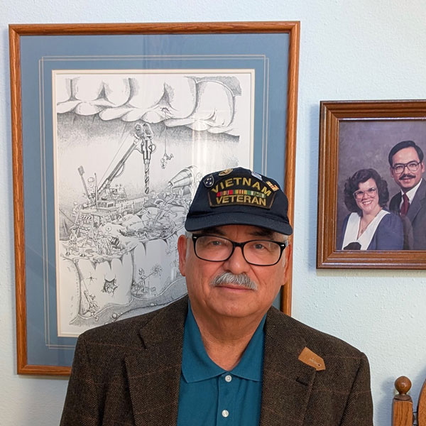 Person wearing a hat reading "Vietnam Veteran" standing indoors in front of framed artwork