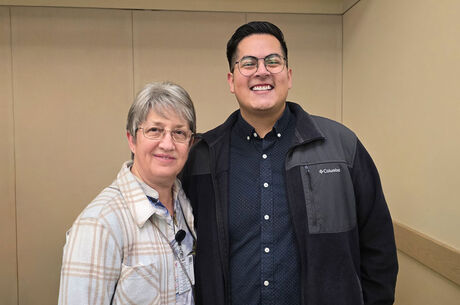 Alisa and Ethan standing side by side indoors at a professional setting, wearing business-casual clothing against a neutral wall