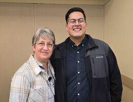 Alisa and Ethan standing side by side indoors at a professional setting, wearing business-casual clothing against a neutral wall