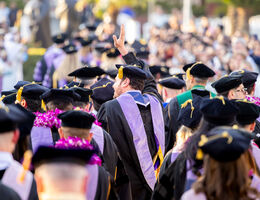Group of LLUSD graduates in caps and gowns at an outdoor commencement ceremony, with one graduate raising a hand.