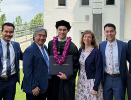 Jason Chan wearing academic regalia holding a diploma folder while standing outdoors with a his family