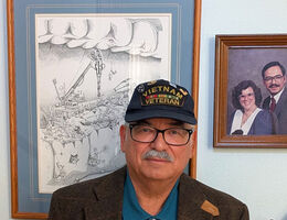 Person wearing a hat reading "Vietnam Veteran" standing indoors in front of framed artwork