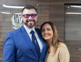 Dr. Vlad Loshkarev and Dr. Laura Mego standing together indoors in front of a School of Dentistry office wall with LLUSD logo in background..