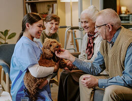 A dental hygiene professional introduces a therapy dog to two elderly patients to help reduce dental anxiety during a visit.